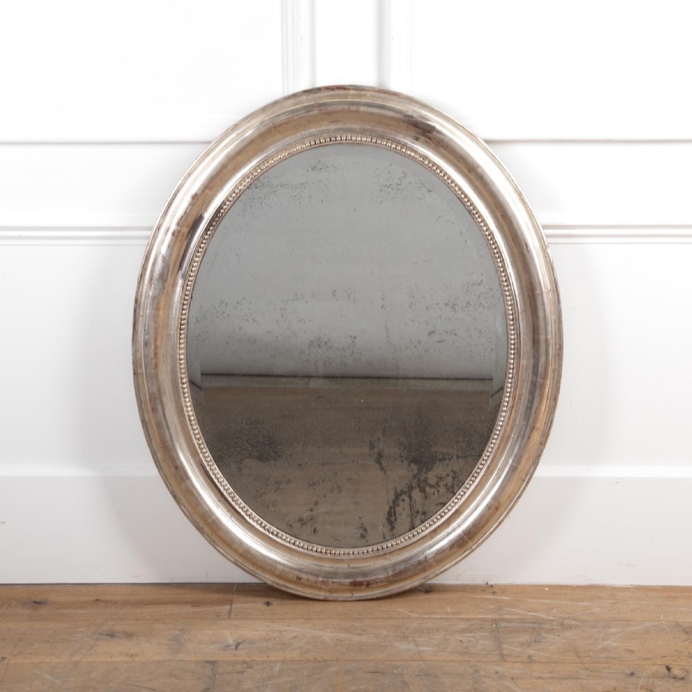 A 19th-century oval wall mirror featuring a silvered moulding frame with beaded rim detail and aged glass showing natural foxing.