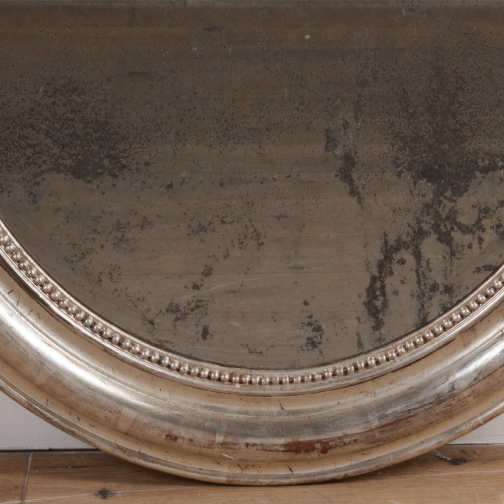 A 19th-century oval wall mirror featuring a silvered moulding frame with beaded rim detail and aged glass showing natural foxing. View II