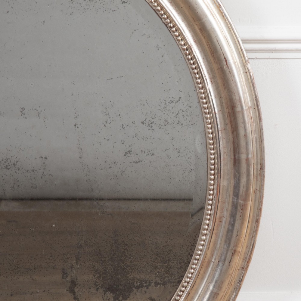 A 19th-century oval wall mirror featuring a silvered moulding frame with beaded rim detail and aged glass showing natural foxing. View IV