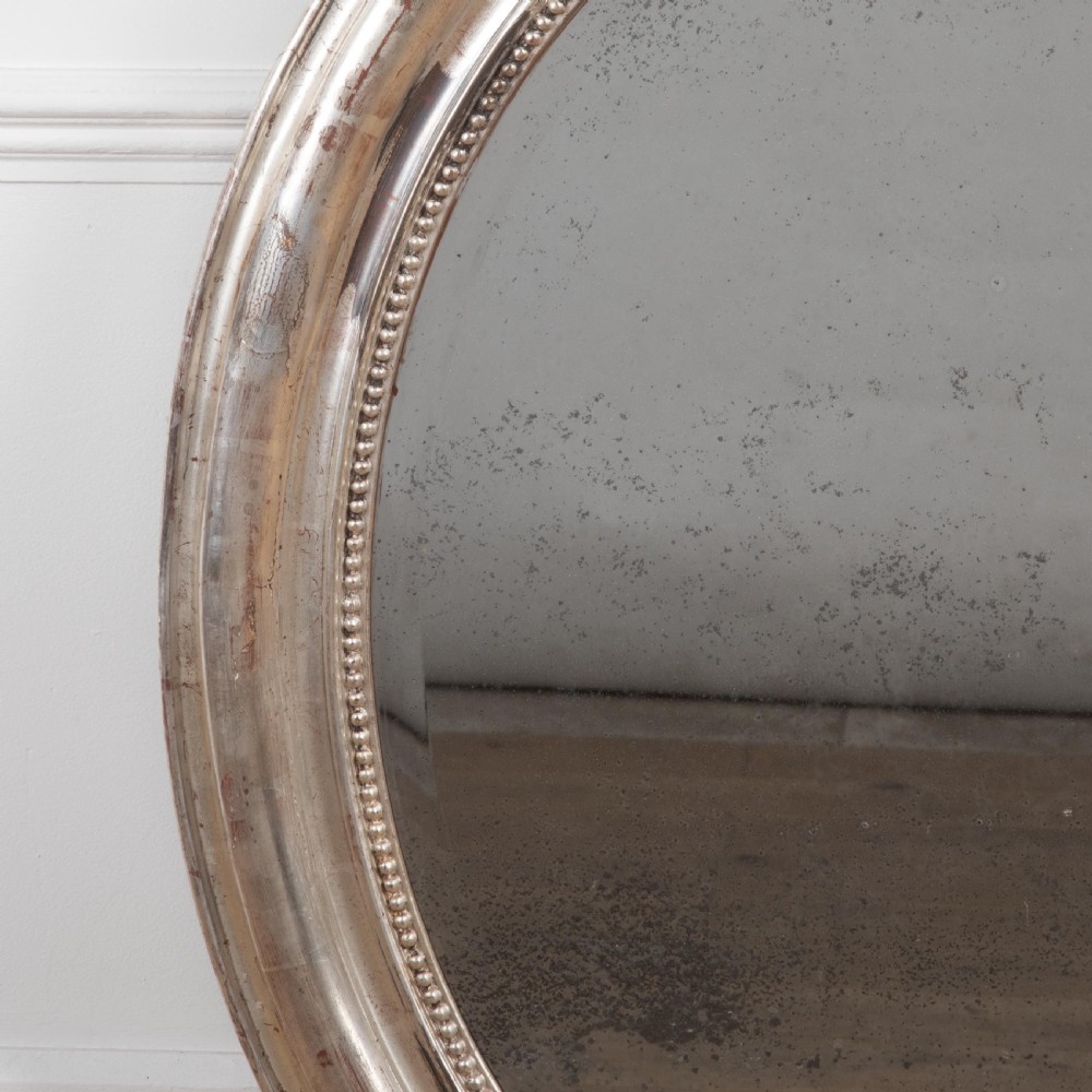 A 19th-century oval wall mirror featuring a silvered moulding frame with beaded rim detail and aged glass showing natural foxing. View V