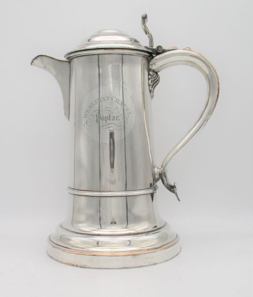 fig 1. A 19th-century silver-plated communion jug featuring a hinged lid, thumbpiece, scroll handle, and an engraved circular emblem reading Wesleyan Chapel Poplar.