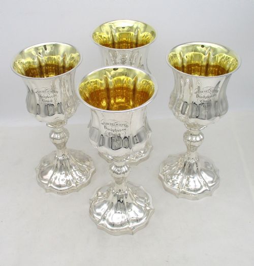 fig 1. A seven-piece silver-plated Victorian communion set featuring two tall lidded flagons, four chalices with gilded interiors, and a shaped waiter tray with church inscriptions.