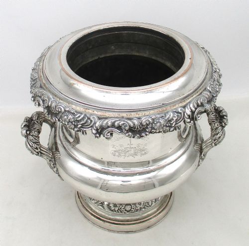 fig 1. A Georgian silver-plated double-handled wine cooler featuring an engraved family crest, foliage borders, and a pedestal base.