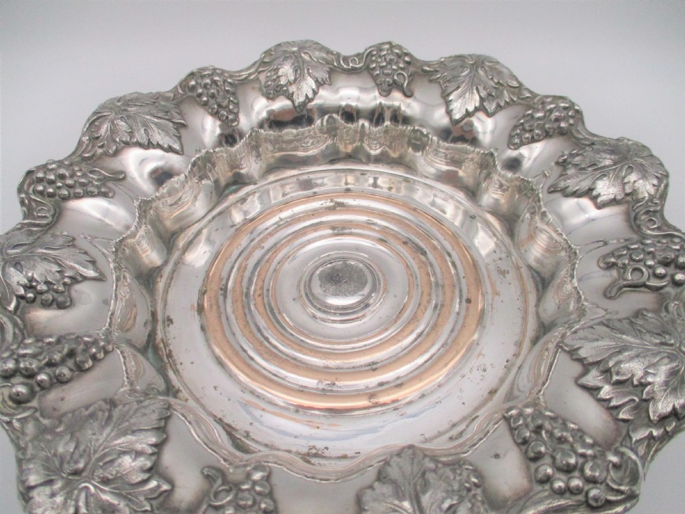 A pair of circular silver-plated wine coasters featuring scalloped rims decorated with grapevine and foliage relief details around concentric circular turned bases. View VIII