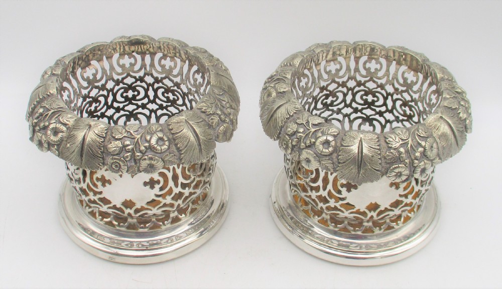 A pair of mid-19th-century silver-plated wine bottle coasters featuring pierced lattice sides, floral repousse borders, and turned wooden bases. View II
