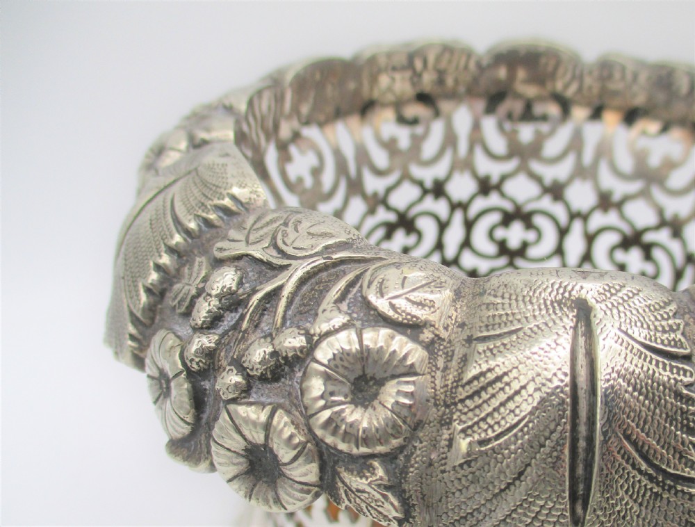 A pair of mid-19th-century silver-plated wine bottle coasters featuring pierced lattice sides, floral repousse borders, and turned wooden bases. View III