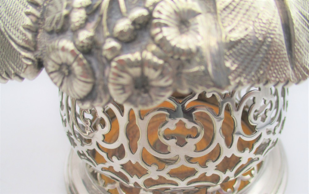 A pair of mid-19th-century silver-plated wine bottle coasters featuring pierced lattice sides, floral repousse borders, and turned wooden bases. View V