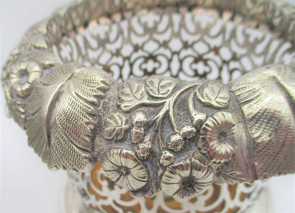 A pair of mid-19th-century silver-plated wine bottle coasters featuring pierced lattice sides, floral repousse borders, and turned wooden bases. View VI