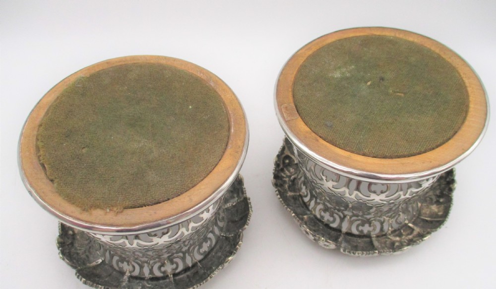 A pair of mid-19th-century silver-plated wine bottle coasters featuring pierced lattice sides, floral repousse borders, and turned wooden bases. View VIII