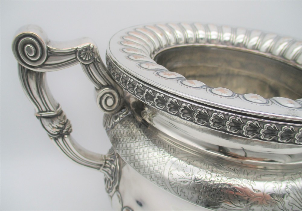 An antique silver-plated urn-shaped wine cooler featuring gadrooned lower details, twin scroll handles, engraved leaf motifs, and subtle copper exposure along worn edges. View II