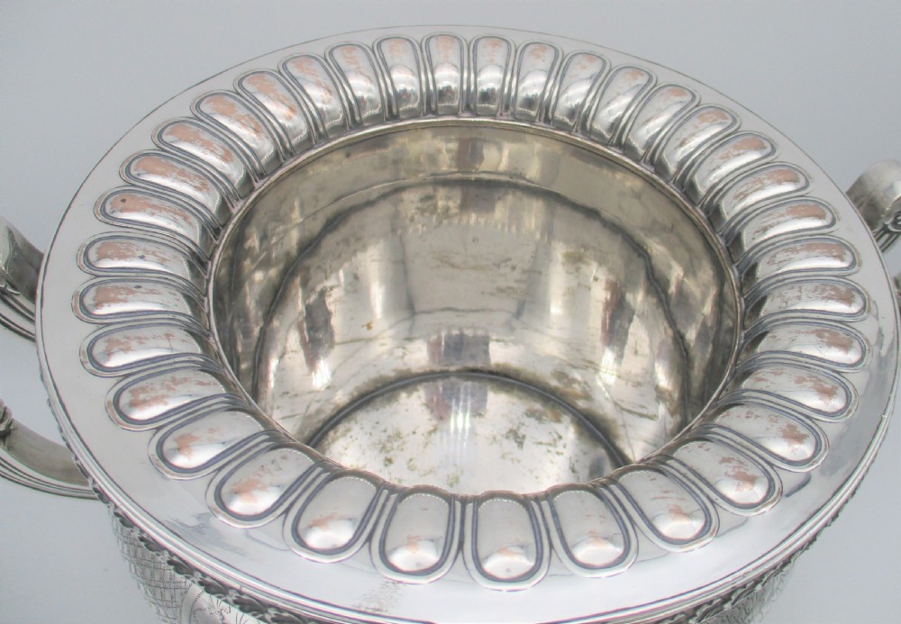 An antique silver-plated urn-shaped wine cooler featuring gadrooned lower details, twin scroll handles, engraved leaf motifs, and subtle copper exposure along worn edges. View III