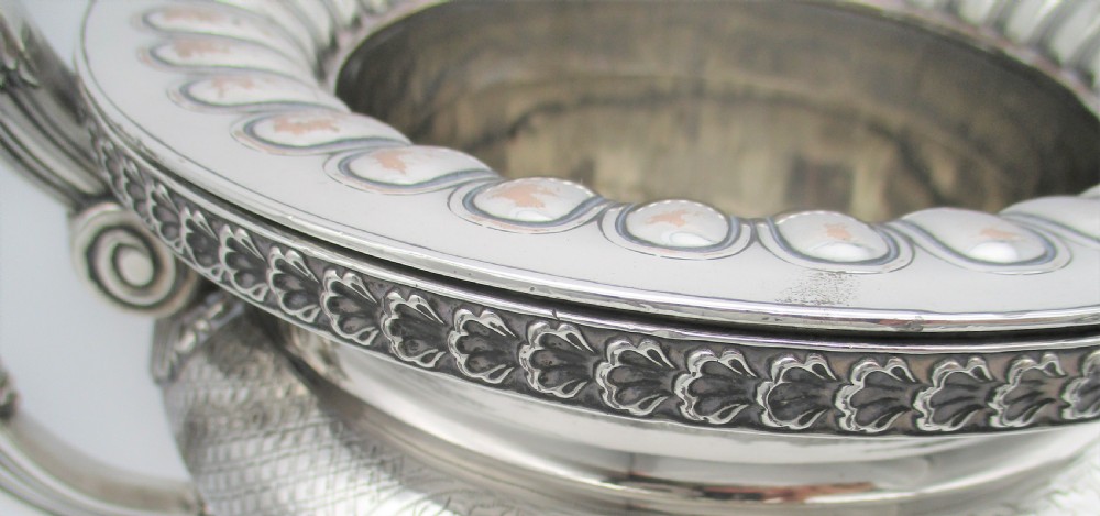 An antique silver-plated urn-shaped wine cooler featuring gadrooned lower details, twin scroll handles, engraved leaf motifs, and subtle copper exposure along worn edges. View IV