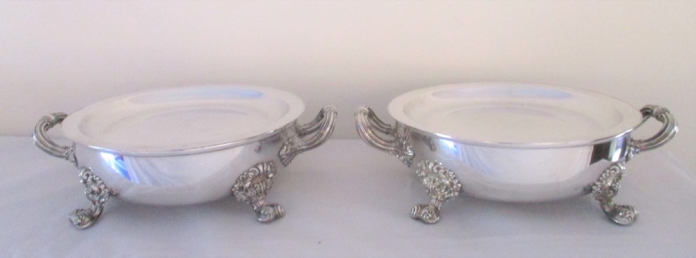 A pair of 19th-century circular silver-plated warming dishes featuring twin handles and ornate cast feet.