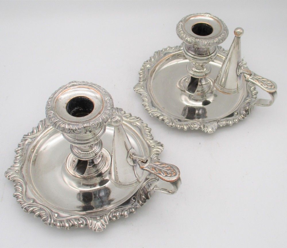 A pair of silver-plated chamber candlesticks featuring wide circular scroll-rimmed bases, integrated finger handles, and removable conical candle snuffers. View II
