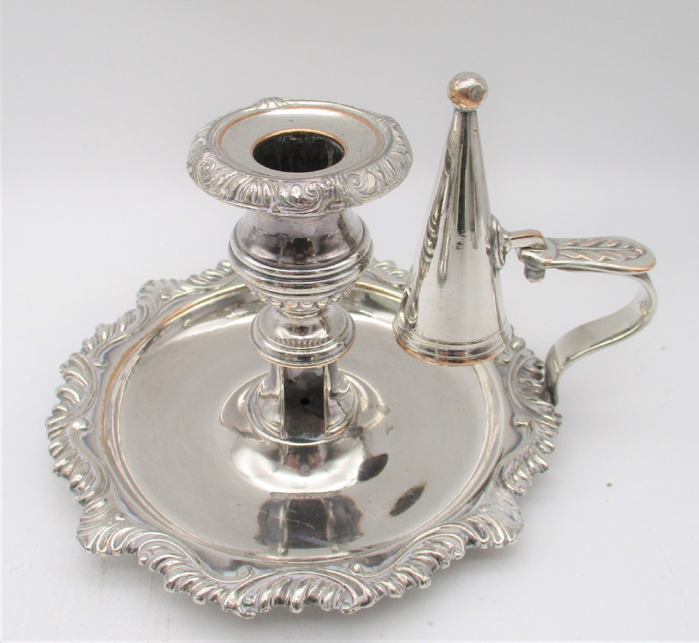 A pair of silver-plated chamber candlesticks featuring wide circular scroll-rimmed bases, integrated finger handles, and removable conical candle snuffers. View III