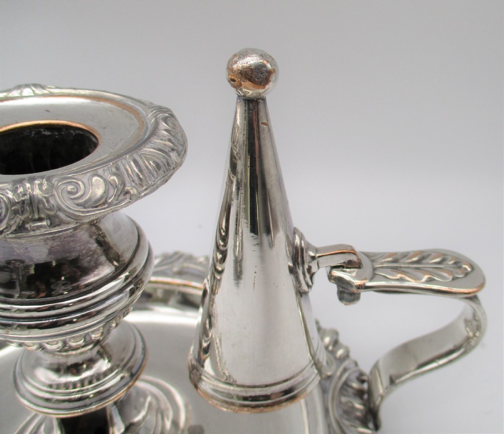 A pair of silver-plated chamber candlesticks featuring wide circular scroll-rimmed bases, integrated finger handles, and removable conical candle snuffers. View IV