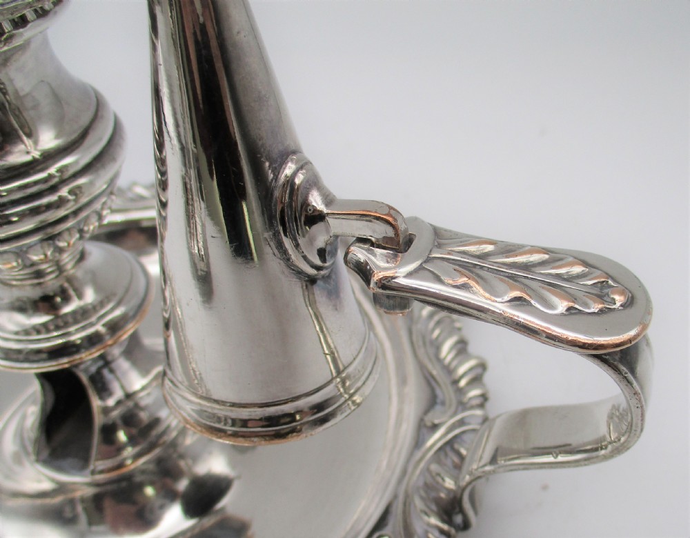 A pair of silver-plated chamber candlesticks featuring wide circular scroll-rimmed bases, integrated finger handles, and removable conical candle snuffers. View VI