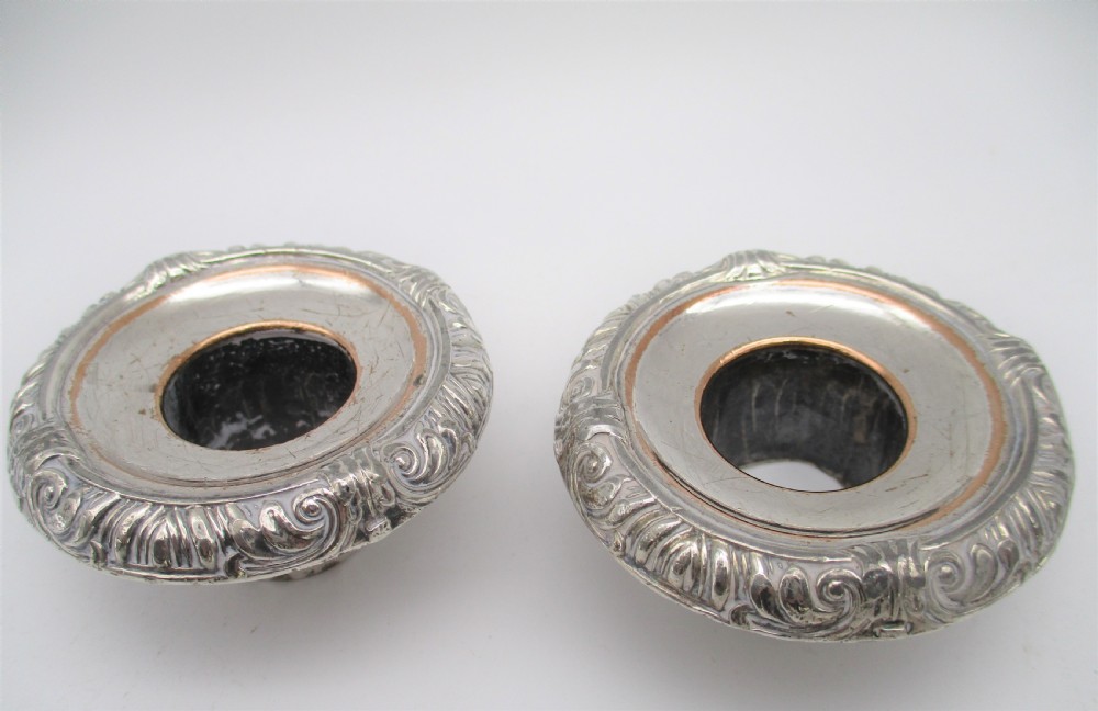 A pair of silver-plated chamber candlesticks featuring wide circular scroll-rimmed bases, integrated finger handles, and removable conical candle snuffers. View VII