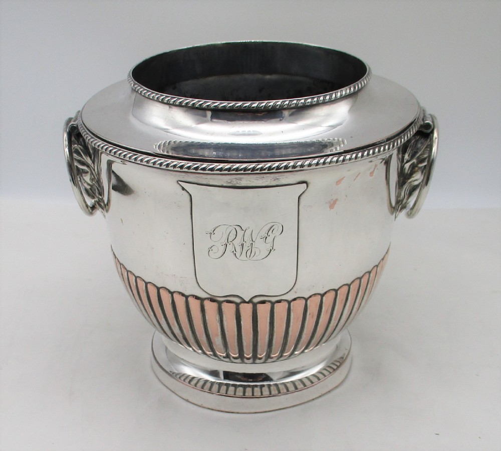 An urn-shaped Old Sheffield Plate wine cooler with a fluted lower body showing copper wear, engraved shield monogram, and gadrooned borders.