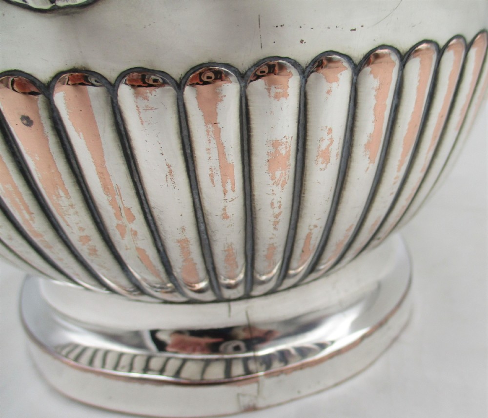An urn-shaped Old Sheffield Plate wine cooler with a fluted lower body showing copper wear, engraved shield monogram, and gadrooned borders. View V