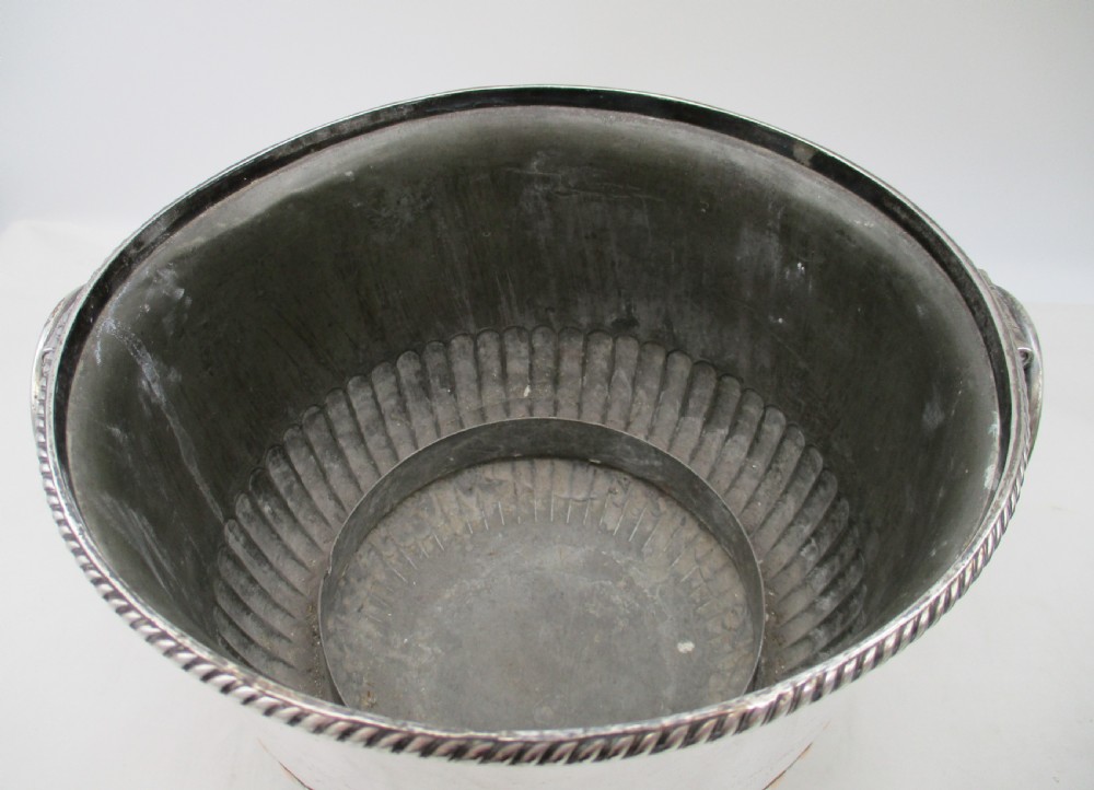 An urn-shaped Old Sheffield Plate wine cooler with a fluted lower body showing copper wear, engraved shield monogram, and gadrooned borders. View VI