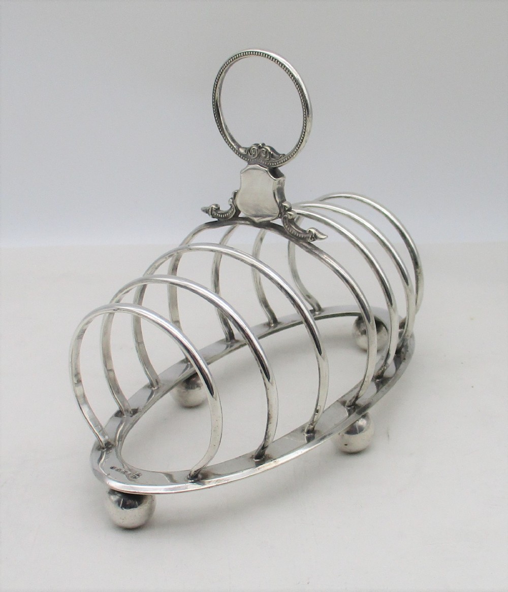 A Victorian silver-plated toast rack featuring arched wire dividers, ball feet, and a central ring handle with scroll decoration.