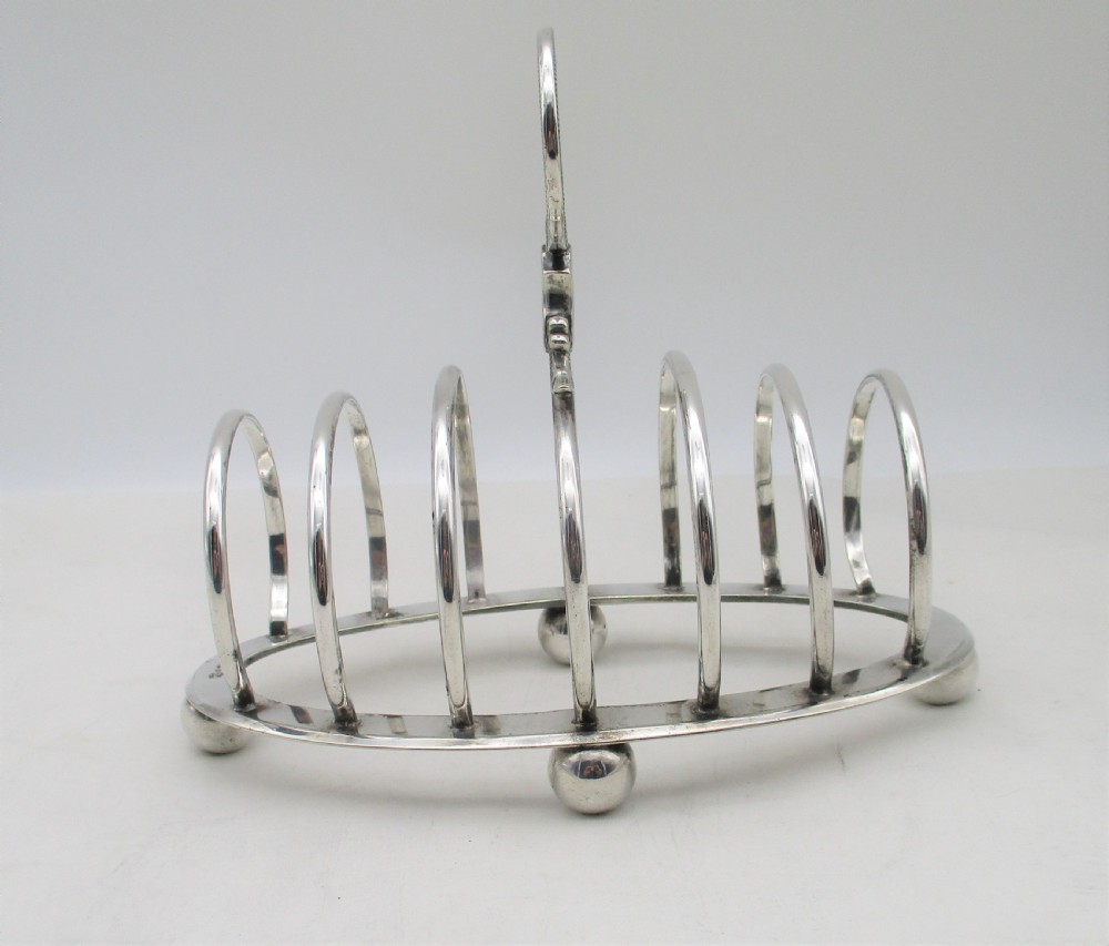 A Victorian silver-plated toast rack featuring arched wire dividers, ball feet, and a central ring handle with scroll decoration. View III