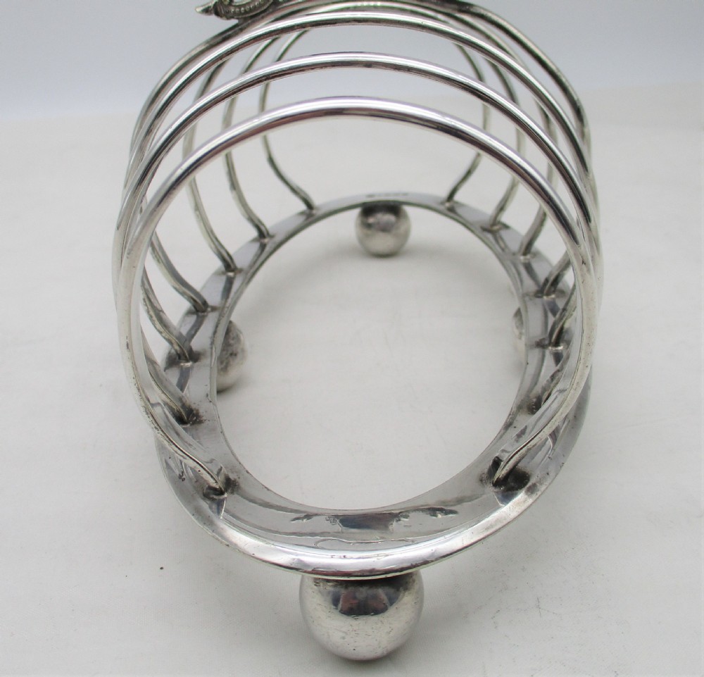 A Victorian silver-plated toast rack featuring arched wire dividers, ball feet, and a central ring handle with scroll decoration. View V