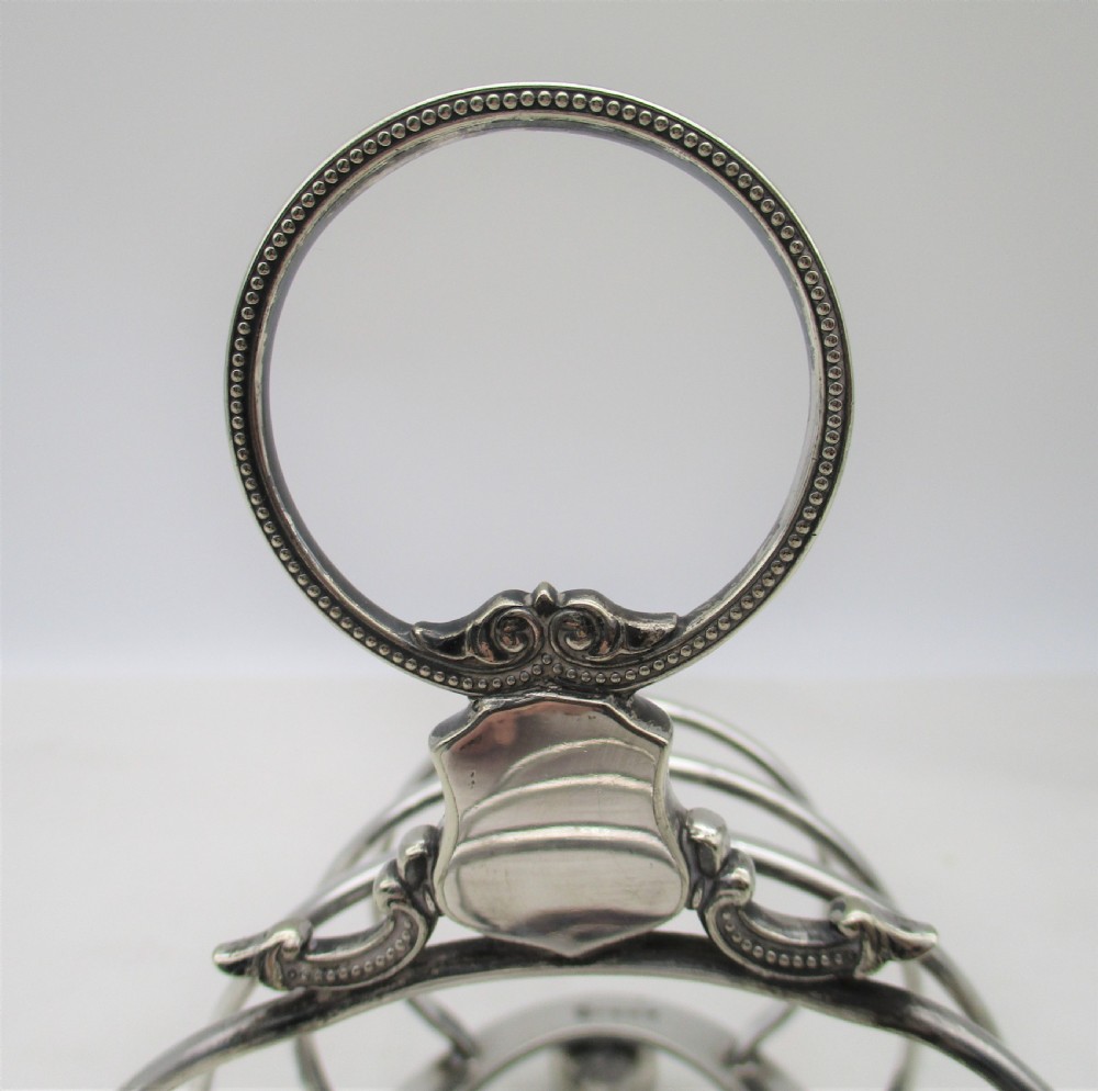 A Victorian silver-plated toast rack featuring arched wire dividers, ball feet, and a central ring handle with scroll decoration. View VI