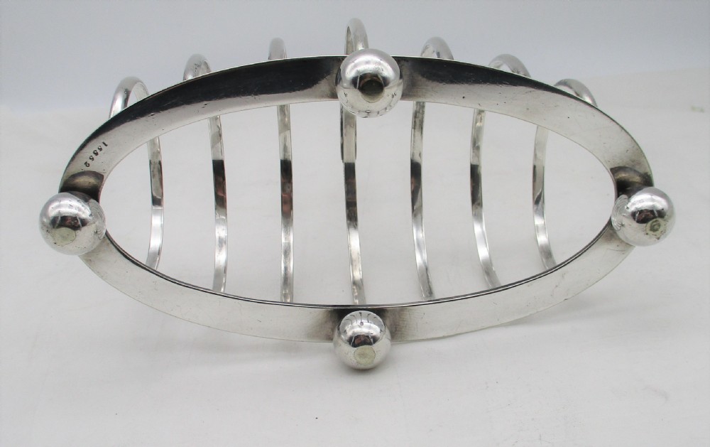 A Victorian silver-plated toast rack featuring arched wire dividers, ball feet, and a central ring handle with scroll decoration. View VIII