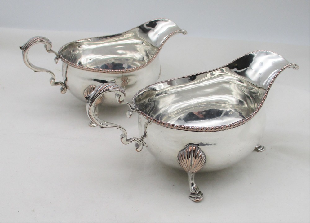 A pair of silver-plated sauce boats featuring double-scroll handles, gadrooned rims, and shell-capped feet.