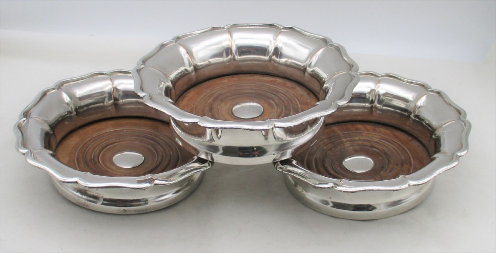 A set of three silver-plated wine bottle coasters with scalloped rims and turned wood bases. View II
