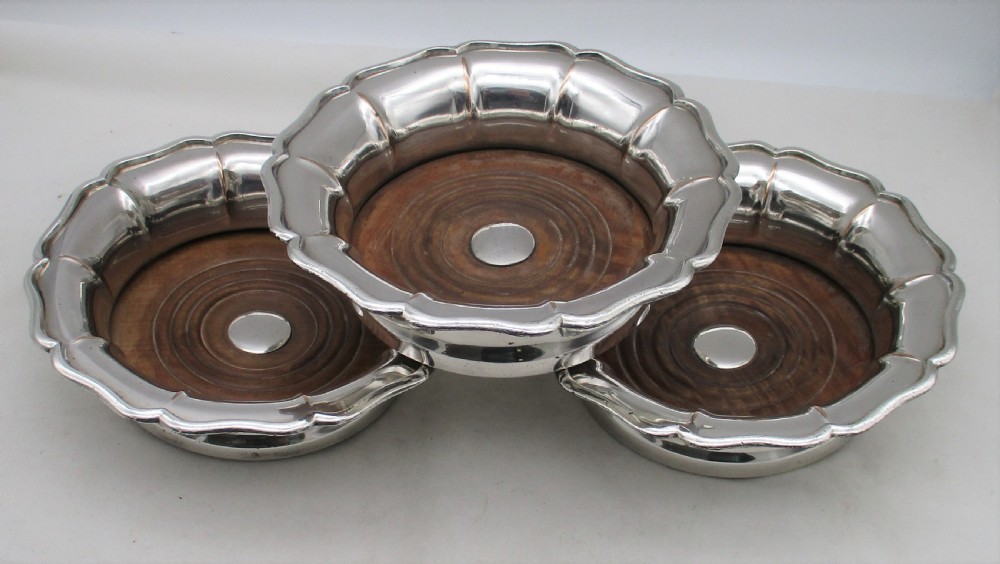 A set of three silver-plated wine bottle coasters with scalloped rims and turned wood bases. View III