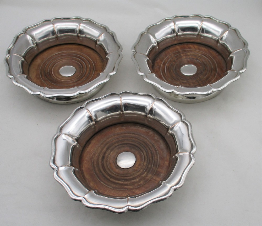 A set of three silver-plated wine bottle coasters with scalloped rims and turned wood bases. View IV