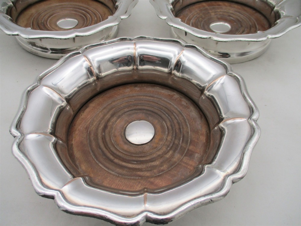 A set of three silver-plated wine bottle coasters with scalloped rims and turned wood bases. View V