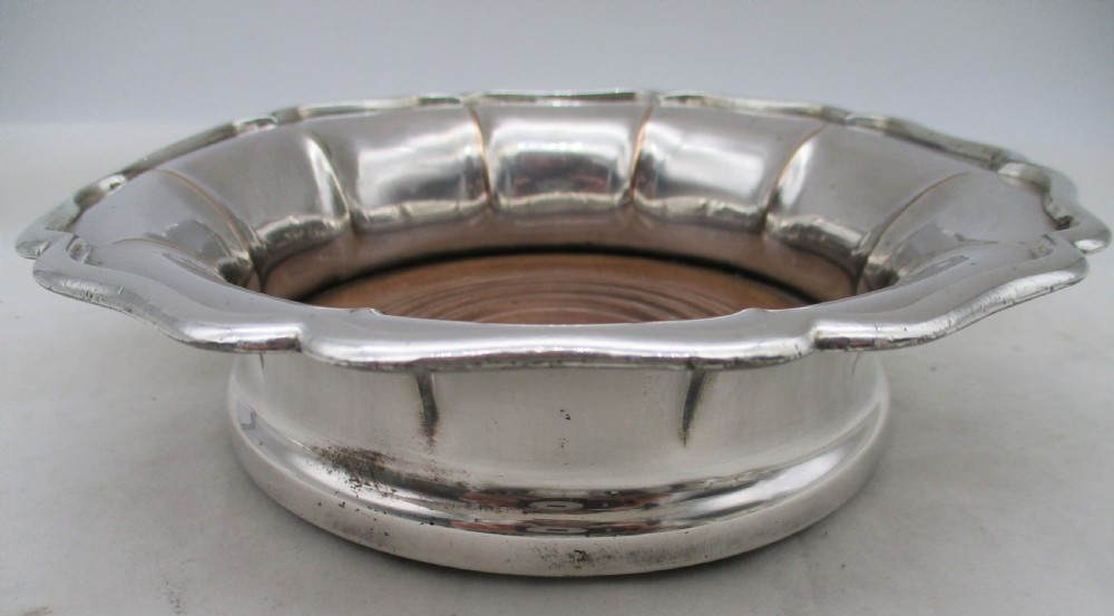 A set of three silver-plated wine bottle coasters with scalloped rims and turned wood bases. View VII