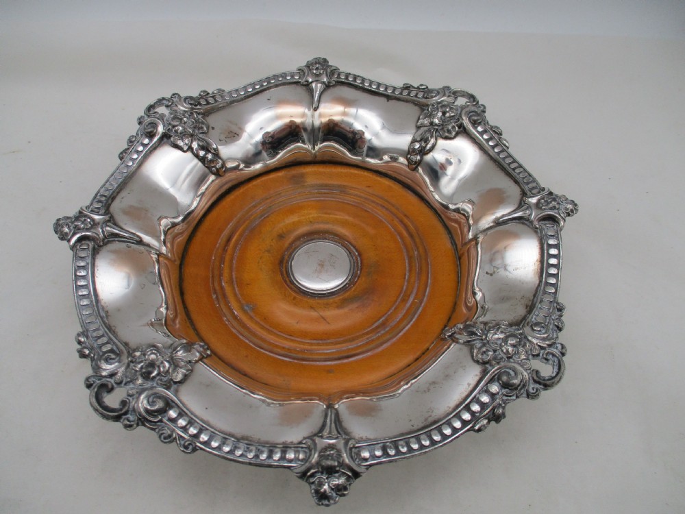 A pair of circular Regency silver-plated decanter coasters featuring turned wooden bases, central silver bosses, and ornate shell and scroll borders. View IV