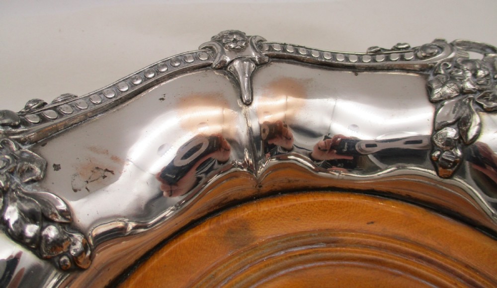 A pair of circular Regency silver-plated decanter coasters featuring turned wooden bases, central silver bosses, and ornate shell and scroll borders. View VI