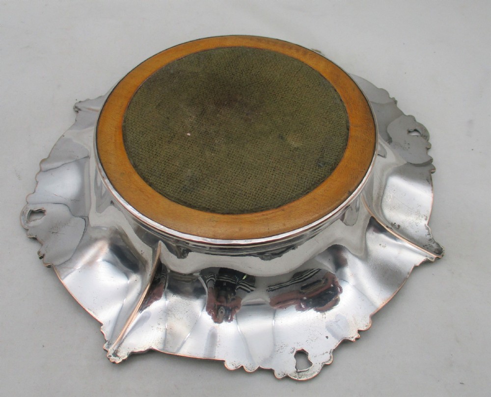 A pair of circular Regency silver-plated decanter coasters featuring turned wooden bases, central silver bosses, and ornate shell and scroll borders. View VII