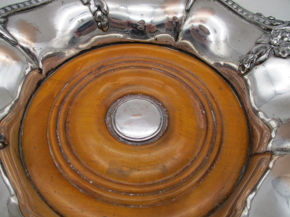 A pair of circular Regency silver-plated decanter coasters featuring turned wooden bases, central silver bosses, and ornate shell and scroll borders. View VIII
