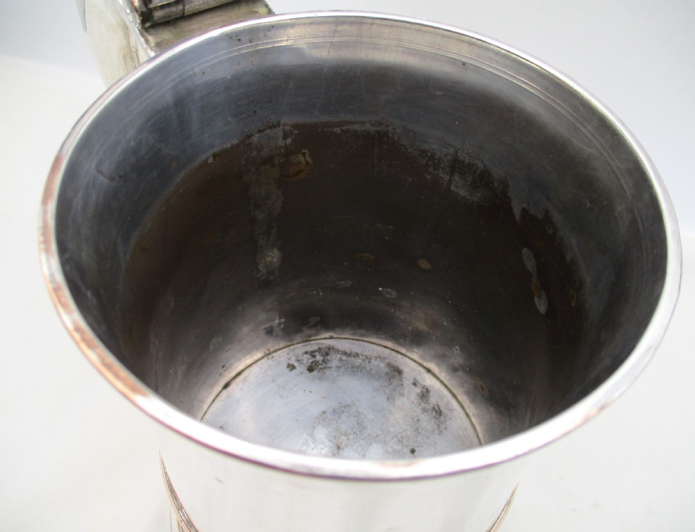 An 18th-century Old Sheffield plated silver quart tankard featuring a domed lid, thumbpiece, scroll handle, and visible copper bleeding along the moulded edges. View VI