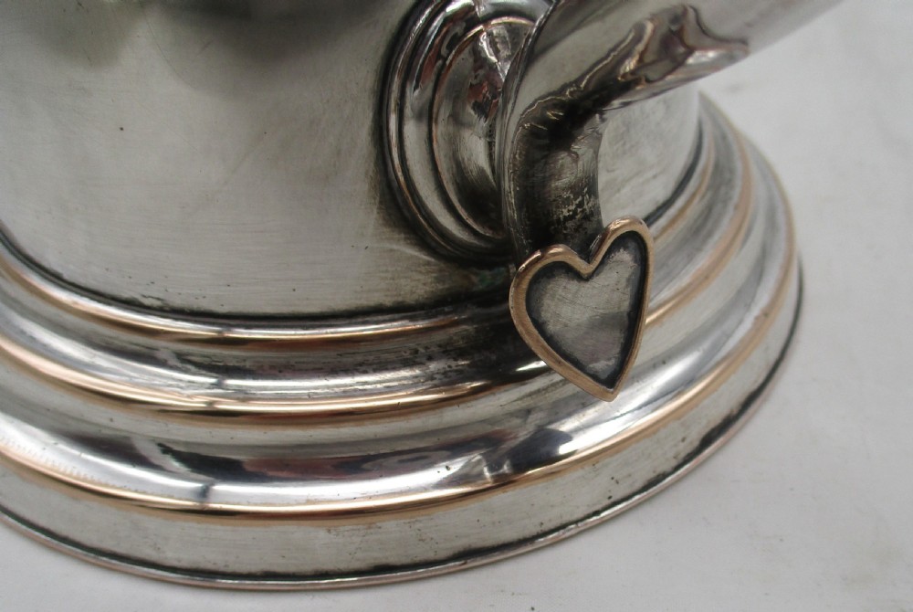 A Georgian silver-plated beer jug featuring a hinged stepped lid, flared base, and curved handle with faint copper oxidisation visible along the edges. View III