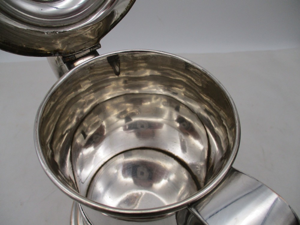 A Georgian silver-plated beer jug featuring a hinged stepped lid, flared base, and curved handle with faint copper oxidisation visible along the edges. View VI