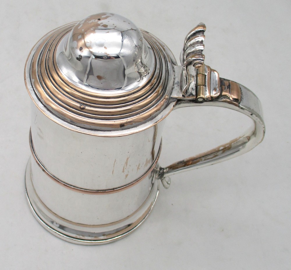 An antique silver-plated lidded tankard showing copper exposure along the rims, featuring a hinged domed lid, thumbpiece, and scroll handle. View II