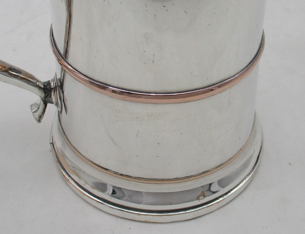 An antique silver-plated lidded tankard showing copper exposure along the rims, featuring a hinged domed lid, thumbpiece, and scroll handle. View V