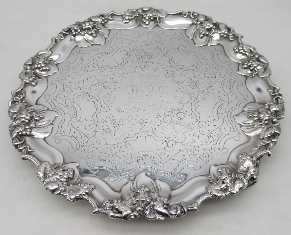 A circular silver-plated tray featuring engraved scrollwork across the surface and a raised border decorated with molded grapevine and foliage motifs. View II