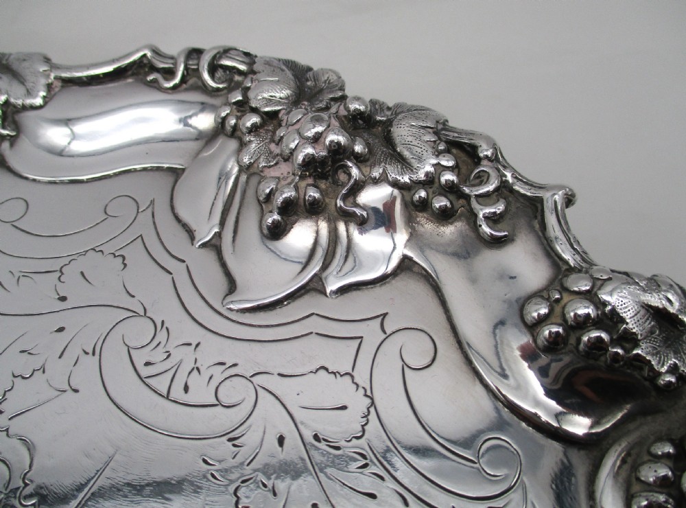 A circular silver-plated tray featuring engraved scrollwork across the surface and a raised border decorated with molded grapevine and foliage motifs. View III