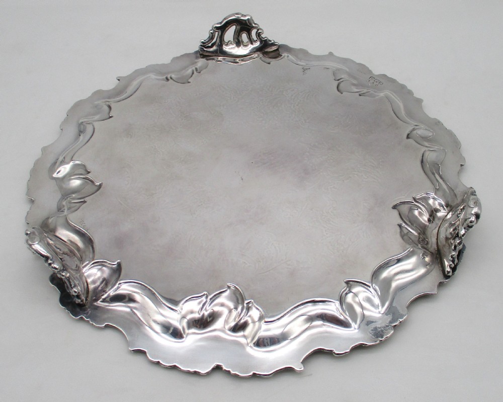 A circular silver-plated tray featuring engraved scrollwork across the surface and a raised border decorated with molded grapevine and foliage motifs. View VII