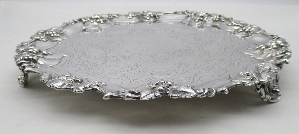 A circular silver-plated tray featuring engraved scrollwork across the surface and a raised border decorated with molded grapevine and foliage motifs. View VIII