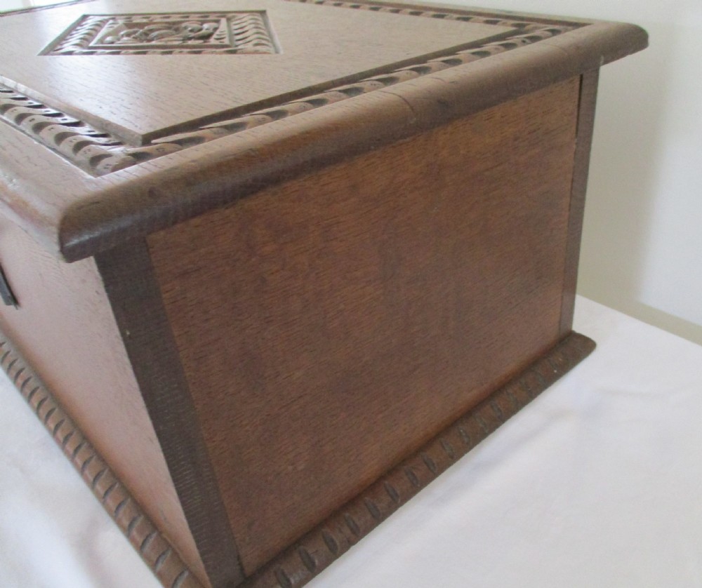 A rectangular carved oak box featuring a flat hinged lid with a carved central lozenge motif, carved borders, and a dark iron lock plate on the front panel. View II